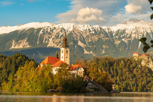 Peaceful sunset view of Lake Bled with the island church and castle reflecting in calm waters, surrounded by soft autumn light and mountain silhouettes