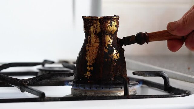 Male hand holding traditional Turkish coffee pot with spilled coffee over gas stove flame
