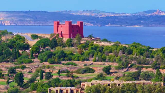 Midday 4K drone parallax over Mellieha Bay from the Red Tower: vivid red fortress, terraced fields, winding road and turquoise sea&mdash;cinematic heritage and landscape footage for travel, tourism