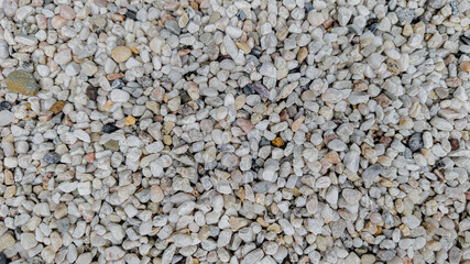 Horizontal macro top view of small light gray and beige stones. Natural pebble texture used for landscaping, gardening, or decorative design. Neutral and calm background with natural stone pattern for