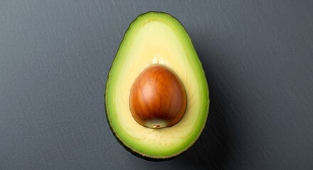 Close up overhead view of a ripe avocado cut in half revealing its smooth brown seed and creamy green flesh on a dark textured surface