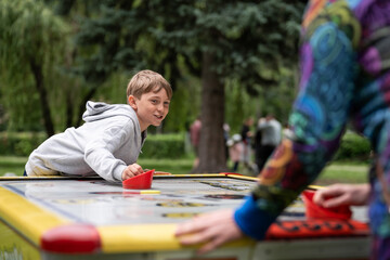 A teenager playing air hockey with a woman (his mother) in the park