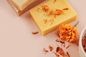 Closeup of yellow handmade soap with dried calendula petals and marigold flower on soft pastel background