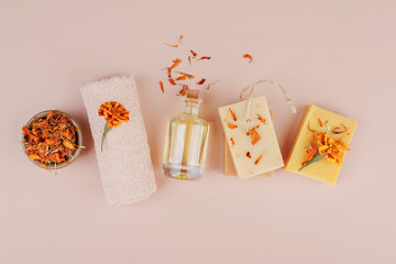 Top view of natural soap bars, dried calendula petals, oil bottle, rolled towel and marigold flower...