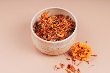 Dried marigold petals in a ceramic bowl with a fresh calendula flower on beige background