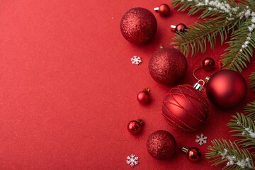Christmas red ornaments and pine branches on red background. Holiday decoration, winter celebration, and festive mood concept. Merry Christmas and seasonal composition background.
