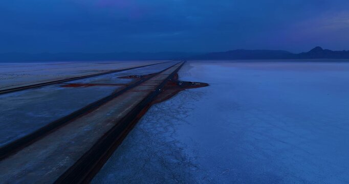 Lonely car rides by the road in the vast salty plain. Footage over the Bonneville Salt Flats, Utah, United States at dusk time.