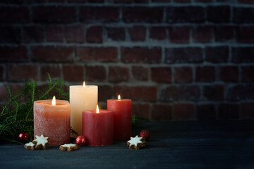 Four candles in warm tones in front of a large cold dark wall, concept for light in the cold night for Christmas, Advent or New Year, copy space, selected focus