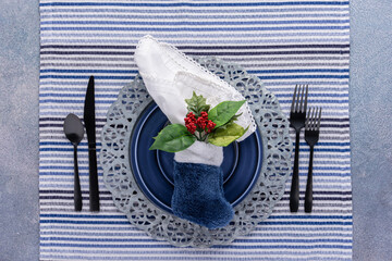 Blue winter holiday place setting. Plate and flatware with white napkin tucked in furry Christmas...