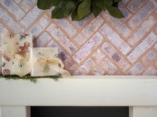 Brick fireplace hearth mantle Christmas holiday festive decoration with wrapped gifts and greenery, hanging green wreath and white wood shelf.