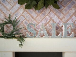 Brick fireplace hearth mantle Christmas holiday festive decoration with Sale letters, hanging green wreath and white wood shelf.
