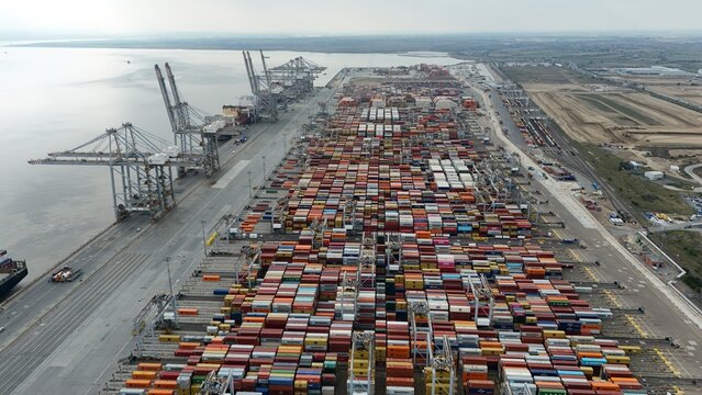 Aerial drone shot wide angle photo of busy shipping port, with gantry trains, cargo containers and transport ships on the River Thames near London, United Kingdom  - Powered by Adobe
