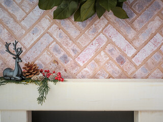 Brick fireplace hearth mantle Christmas holiday festive decoration with black deer and greenery, hanging green wreath and white wood shelf.
