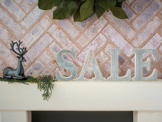 Brick fireplace hearth mantle Christmas holiday festive decoration with Sale letters and black deer, hanging green wreath and white wood shelf.