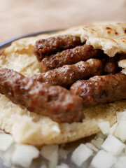 Crispy grilled cevapcici, served in flatbread with fresh, chopped onions on a rustic plate.