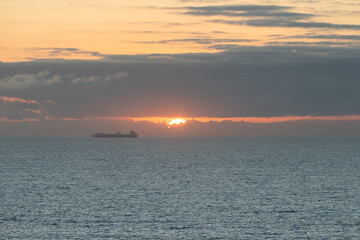 Beautiful sunset over ocean with cargo ship sailing near horizon in calm waters
