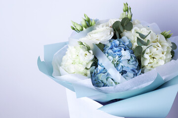 Elegant bouquet of white roses and blue hydrangeas with eucalyptus leaves, wrapped in pastel blue paper
