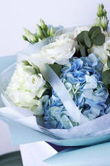 Elegant bouquet of white roses and blue hydrangeas with eucalyptus leaves, wrapped in pastel blue paper
