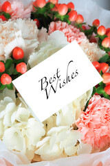 Floral bouquet with pink carnations, white hydrangeas, red berries, and a 'Best Wishes' greeting card