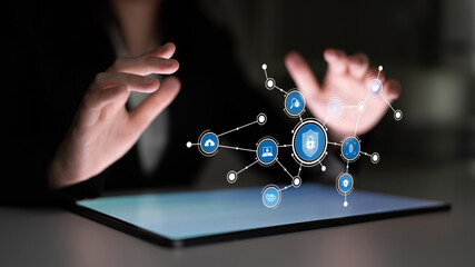 Hands interact with a tablet displaying futuristic security icons, representing digital data protection and networking in a modern and dark environment. Tessel