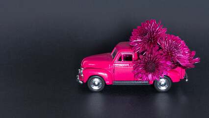Cute old pink car carry violet flowers on black paper background