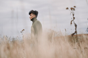 A young man in a turtleneck stands in a windswept field, captured with authentic, documentary style...