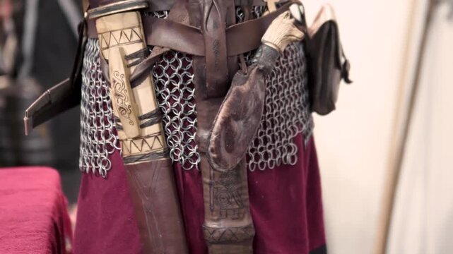 Scene of a medieval warrior donning his armor and accessories, preparing for battle. Dressing in his clothing, seen in his hands: belt, knives, chainmail.