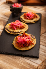 Panuchos, a typical dish from Yucatan, Mexico. A handmade, fried corn tortilla filled with beans, topped with cochinita pibil, pickled red onion, and habanero pepper.