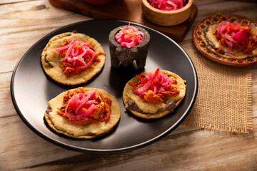 Panuchos, a typical dish from Yucatan, Mexico. A handmade, fried corn tortilla filled with beans, topped with cochinita pibil, pickled red onion, and habanero pepper.