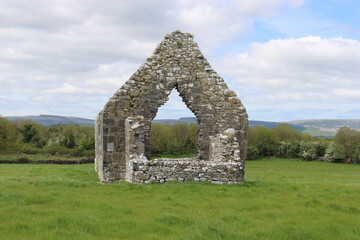 Single ruin in a grassy field at the abandoned Kilmacduagh monastery in Gort, County Ireland