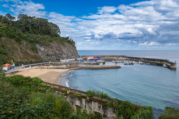 Fototapeta premium Lastres, Spain – View of the harbor and beach in Asturias, showing fishing boats, calm waters, and the coastal charm of this picturesque seaside village.