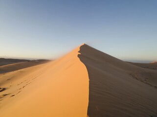 Golden sand dune illuminated by sunlight against a clear blue sky.
