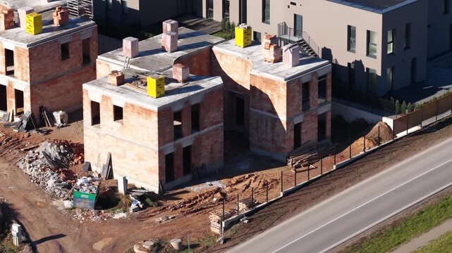 Drone image showing multiple two-story brick houses in early construction stages with exposed walls, concrete slabs, and construction materials on site.
