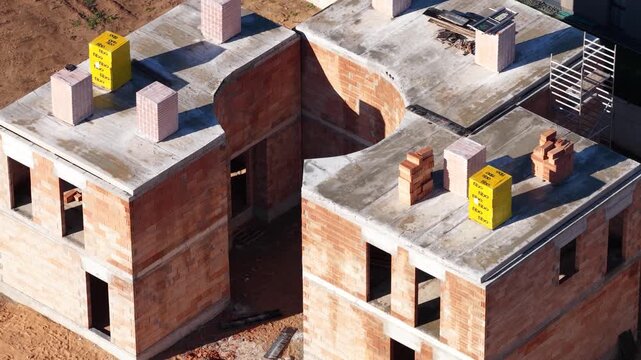 Drone image showing multiple two-story brick houses in early construction stages with exposed walls, concrete slabs, and construction materials on site.