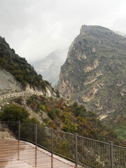 Misty mountain peak with wet wooden deck and stone path, autumn trees and clouds creating dramatic hiking and exploration atmosphere.