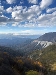 Naklejka premium Mountain valley with autumn trees, rocky slopes, and dramatic clouds