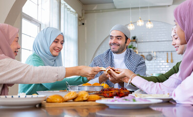 Middle eastern muslim housewife lady in hijab is serving naan bread to family dining table with her husband and relatives during Eid Mubarak, Ramadan festival for feast and gathering