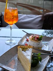 Summer fun: an orange cocktail and two exquisite desserts on a glass table