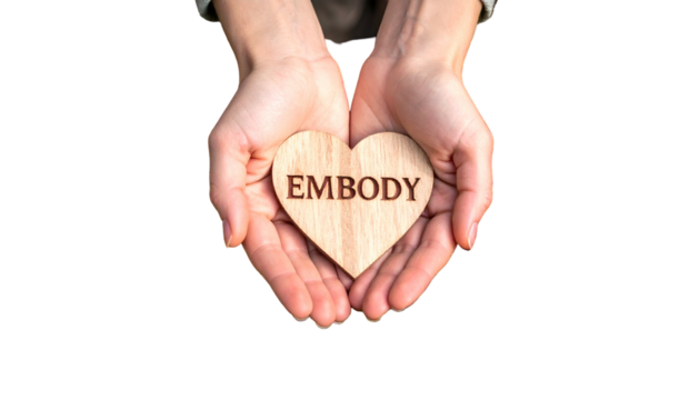 Person cupped hands holding a wooden heart with "EMBODY" etched. Black background