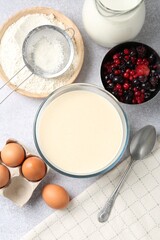 Liquid dough in bowl, berries and ingredients on light grey table, flat lay