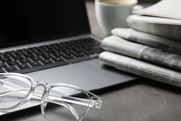 Newspapers, laptop and glasses on grey table, closeup