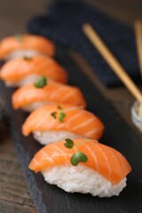 Delicious nigiri sushi with salmon and microgreens on wooden table, closeup