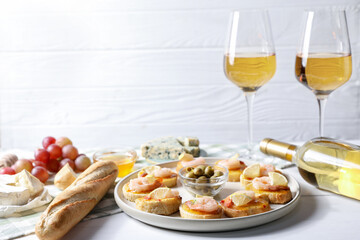 Tasty bruschettas with shrimps, lemon, olives and white wine on light wooden table, closeup