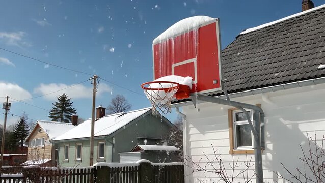 basketball goal system covered in frozen precipitation  with a brightly colored backboard fixed to a snow-laden rooftop under the illumination of a sunny cold-season