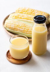 Sweetcorn milk in glass and bottle with fresh sweetcorn on white background, Alternative milk from plant, dairy free