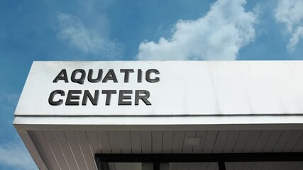 Aquatic Center word sign displayed on the exterior of a modern recreation building with a clear blue sky background, symbolizing swimming, water sports, fitness, and community activity