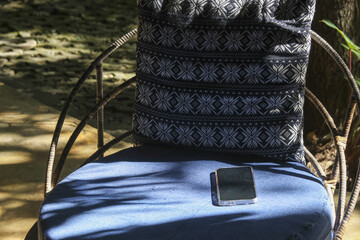 Smartphone on blue cushion chair in peaceful outdoor garden setting. Bright sunlight casts relaxing...