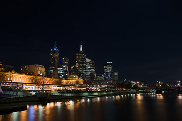 Yarra River, Melbourne CBD, Australia, Wide night cityscape view of the CBD skyline, Flinders Street Station, and St Paul's Cathedral, with strong light reflections on the calm water.