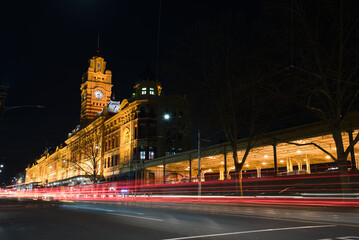 Melbourne, Australia, Night view of the historic Flinders Street Station with its iconic clock tower, featuring light trails from passing traffic on Flinders Street.