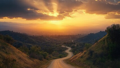 Fototapeta premium Winding road through green hills leading into a valley under a dramatic sunset sky with rays of sunlight breaking through dark clouds